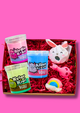 A box of three different coloured jars of sensory putty with three different fidget toys on a light pink background