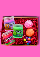 Box with three jars of different coloured cloud putty and three fidget toys on a pink background