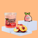 Duo peach sensory putty on a plinth, collectable charm Poppy Peach to the side, with some peach showcasing the scent