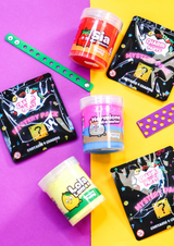 Three jars of colourful sensory putty with three bags of mystery croc charm bags around on a purple and yellow background