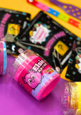 a close up of a pink jar of cloud putty against blurred packs of croc charm bags