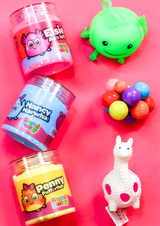 three jars of different coloured cloud putty and three different fidget toys in columns on a pink background