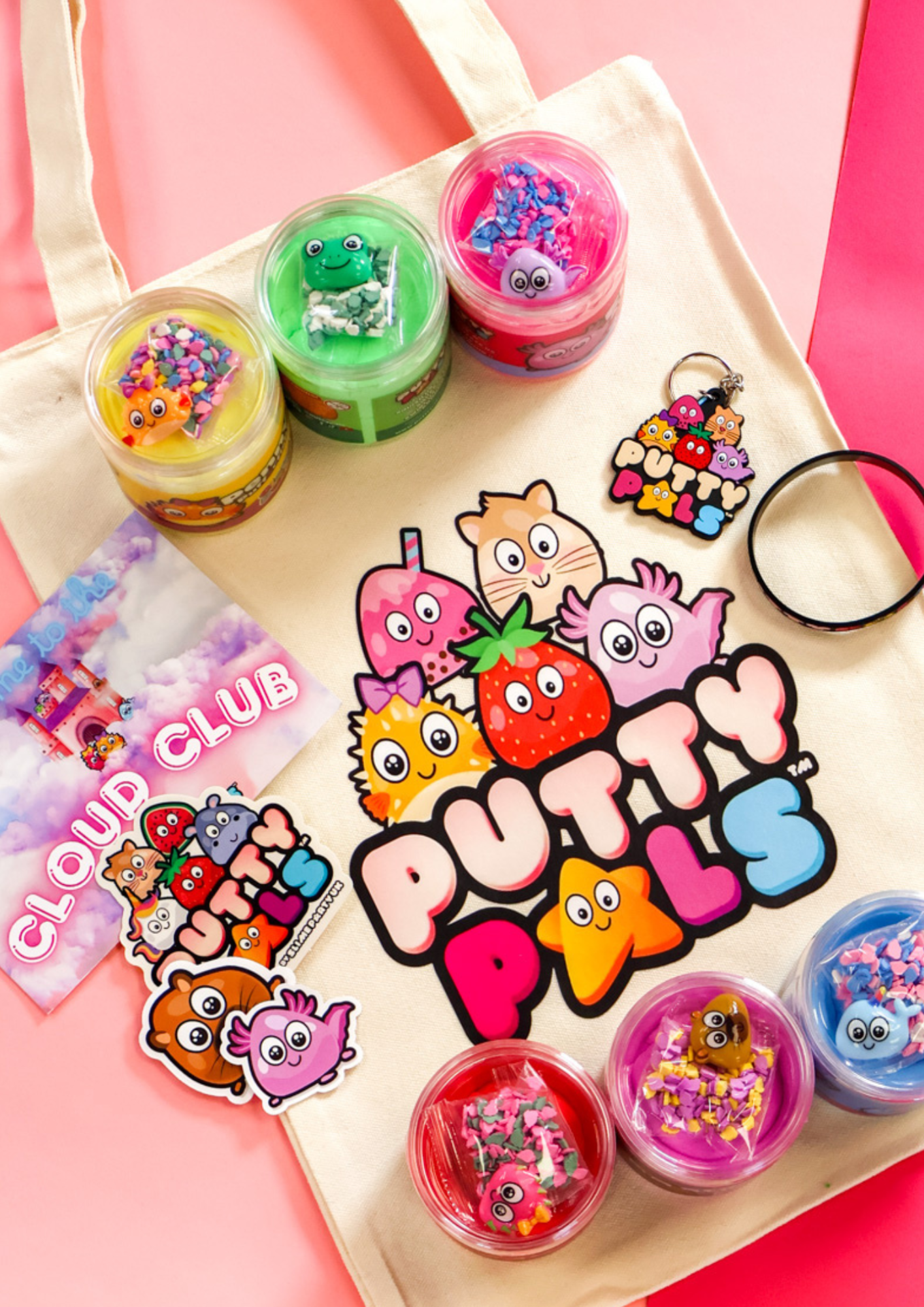 Six jars of colourful cloud putty on a tote bag with the Putty Pals logo on it. Character stickers, keyring and a bracelet are all laid on the bag.