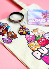 Close up of a tote bag with Putty Pals logo with character stickers, keyring and a bracelet are on the bag.