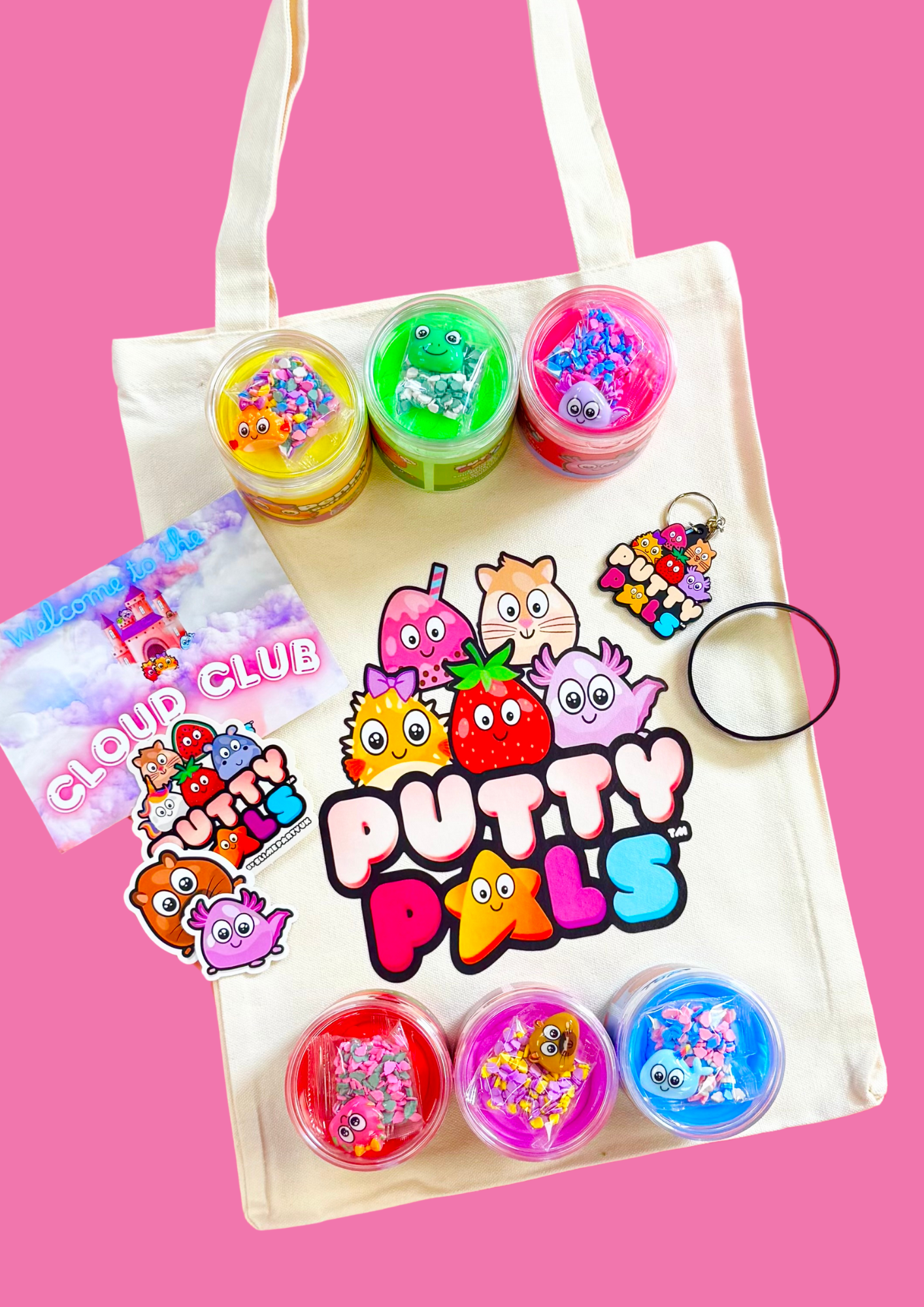 A tote bag with the Putty Pals logo laid flat with 6 jars of colourful putty on it. Alongside stickers, a keyring and a bracelet are also laid on it.