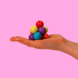 A hand holding a multicoloured atom fidget toy on a pink background