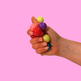 A hand playing with a multi coloured atom fidget toy against a pink background