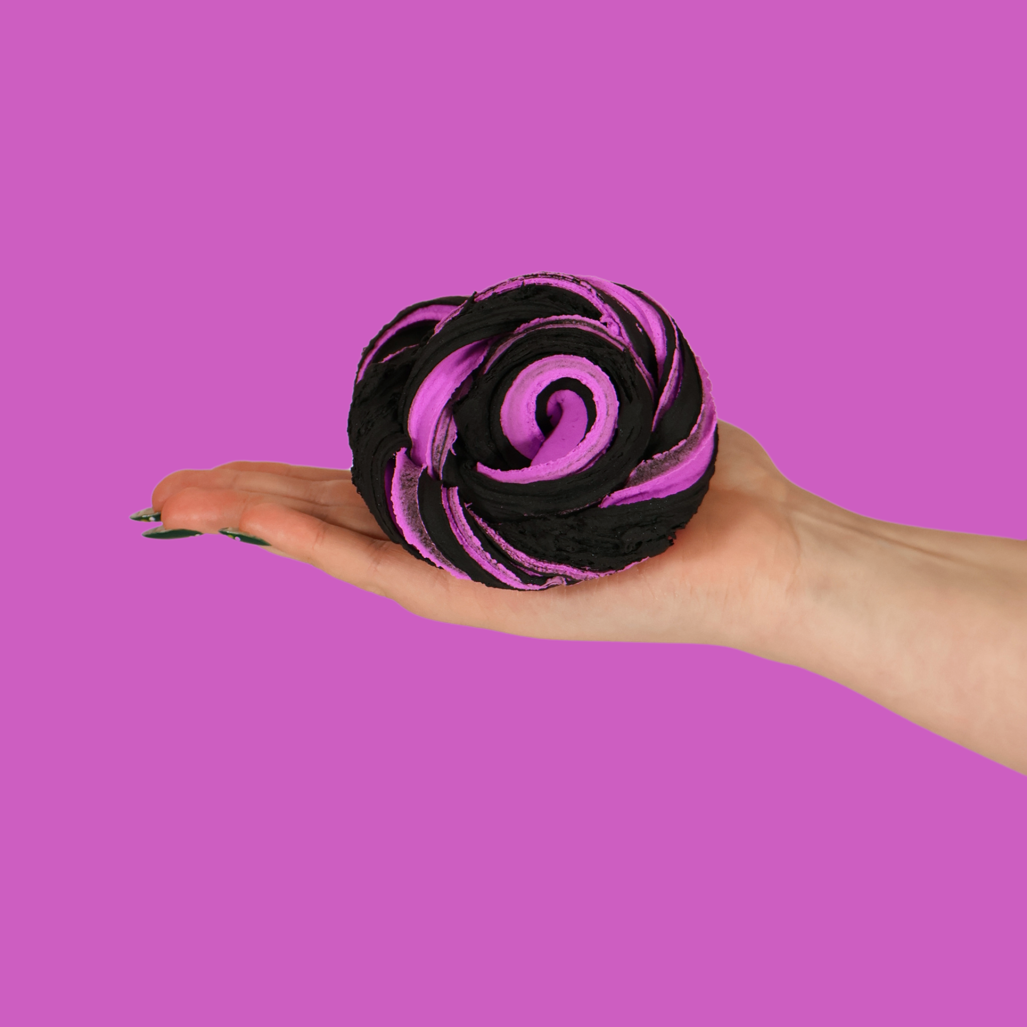 A hand holding a purple and black swirl of sensory putty, on a purple background