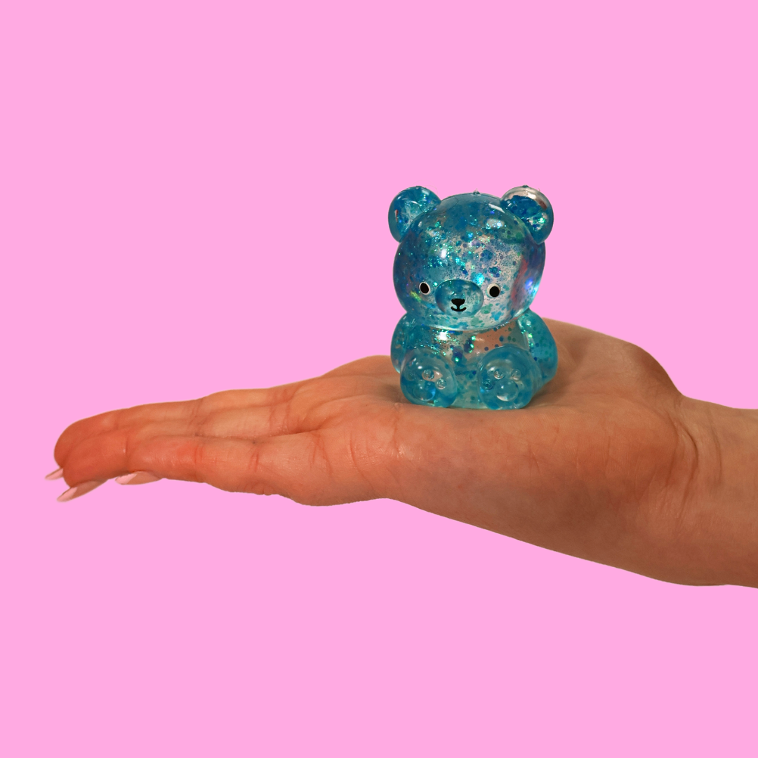 A blue sugar filled fidget toy in the shape of a bear, in the palm of a hand against a pink background