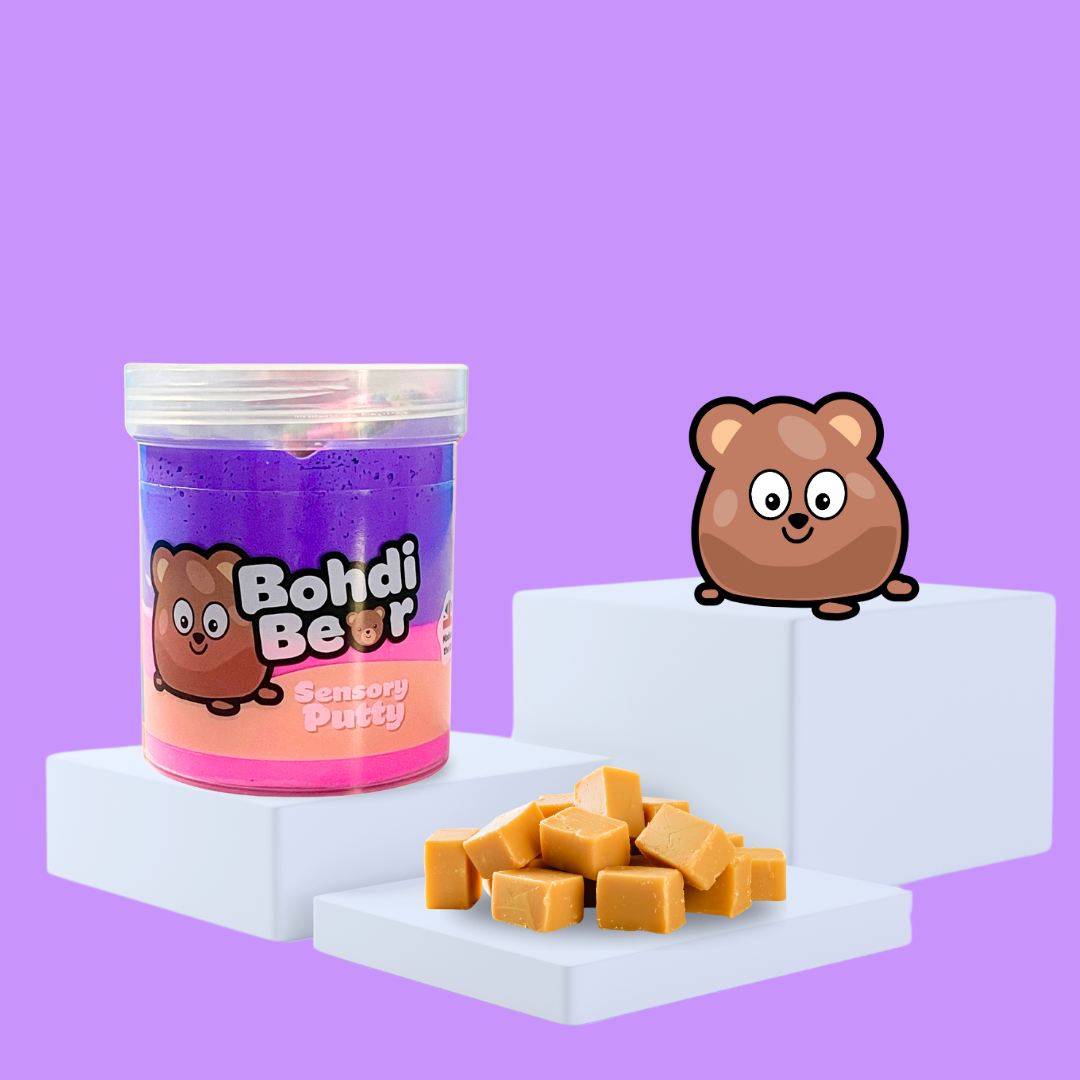 Duo pink and purple sensory putty on a plinth, collectable charm Bohdi Bear to the side, with some caramel showcasing the scent