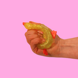 A yellow sugar filled fidget toy in the shape of a duck being squished in a hand, against a pink background