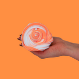 A hand holding a swirl of sensory putty that is white and orange, with an orange background