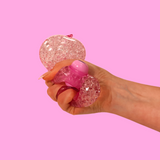 A big orbs filled, pink narwhal fidget toy being squeezed in a hand against a pink background