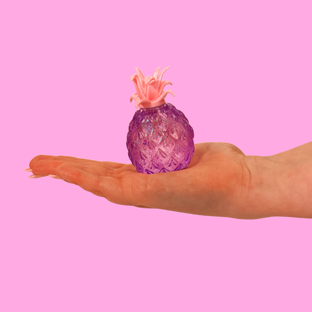 A purple pineapple shaped fidget toy in the palm of a hand, against a pink background