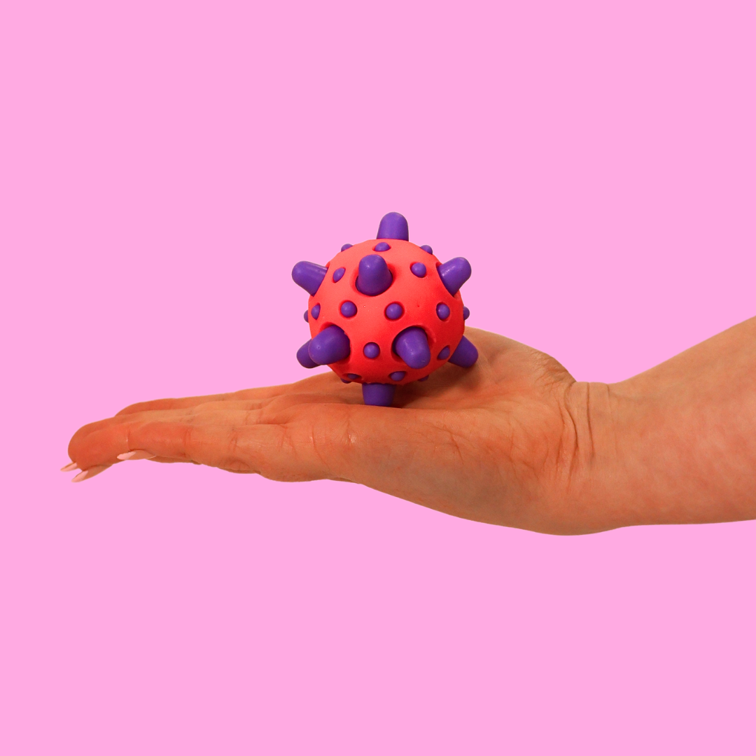 A pink and purple spikey fidget toy ball in the palm of a hand against a pink background