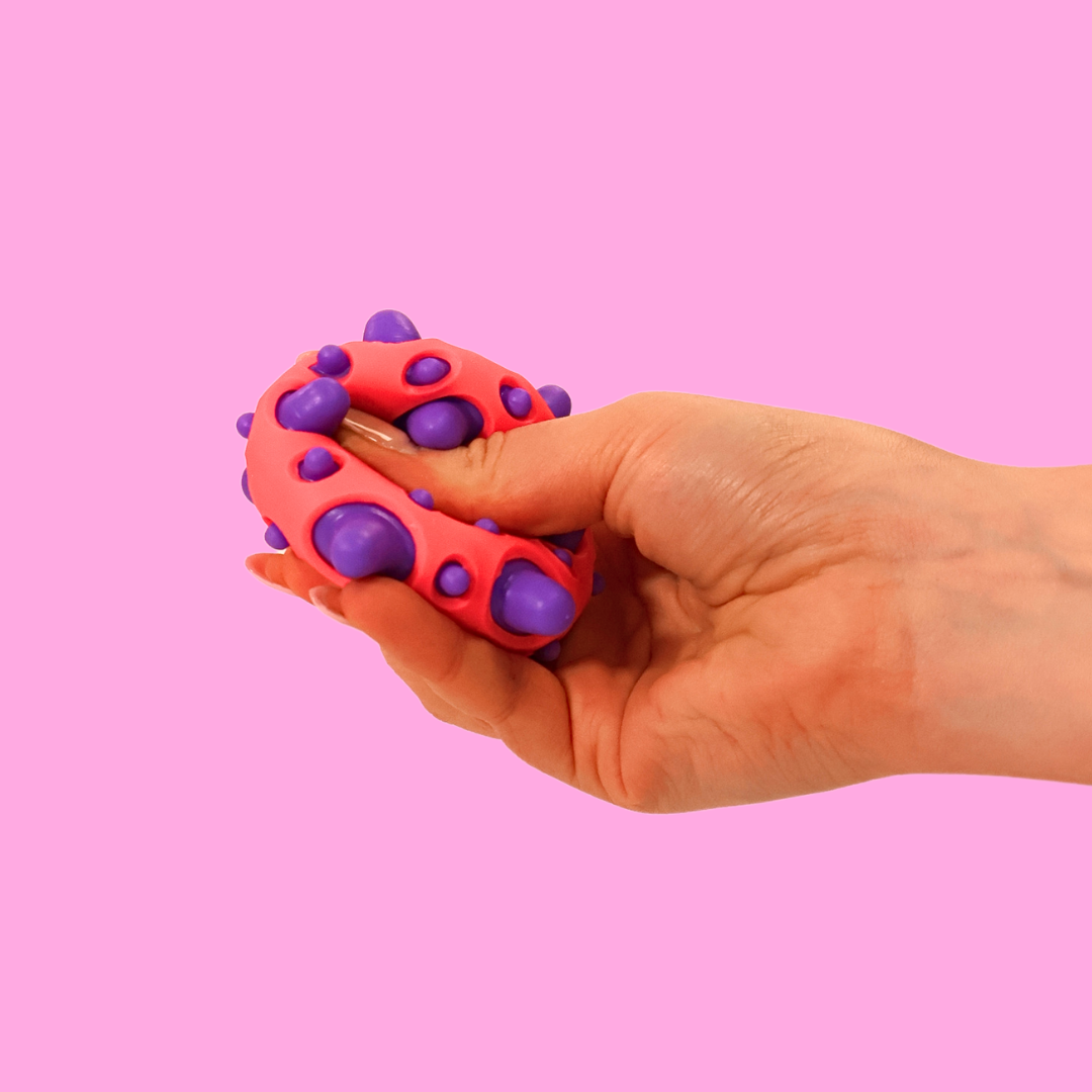 A pink and purple spikey ball being squashed in a hand against a pink background