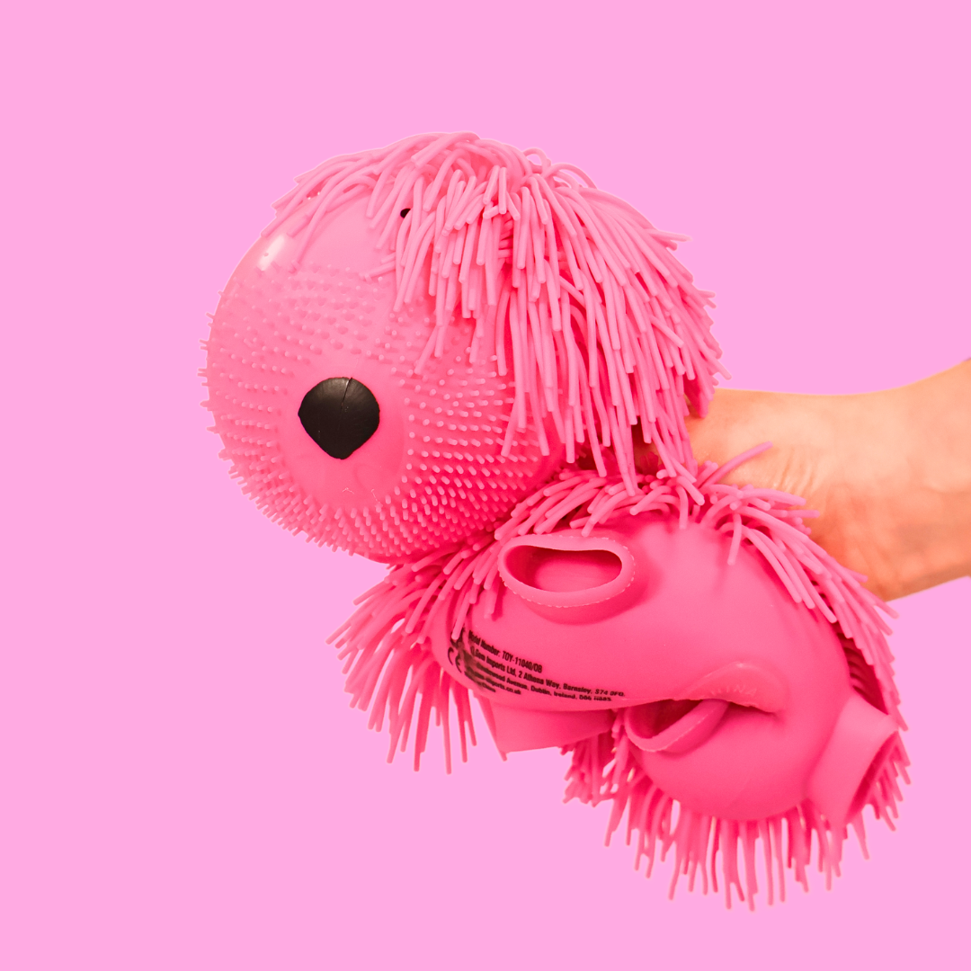 Large pink squishy dog being squashed by a hand, on a pink background