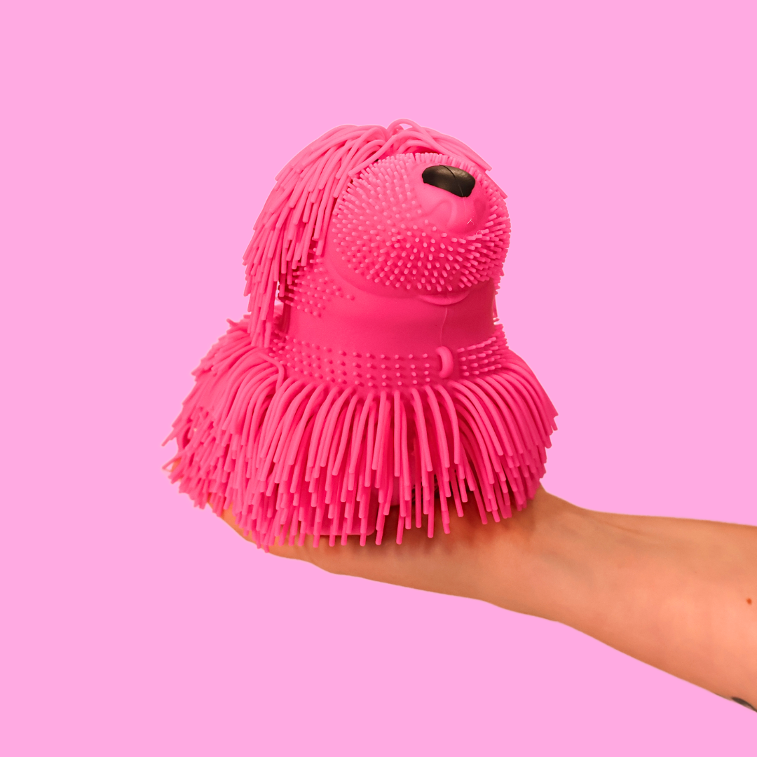 large pink shaggy squishy dog on a hand, against a pink background