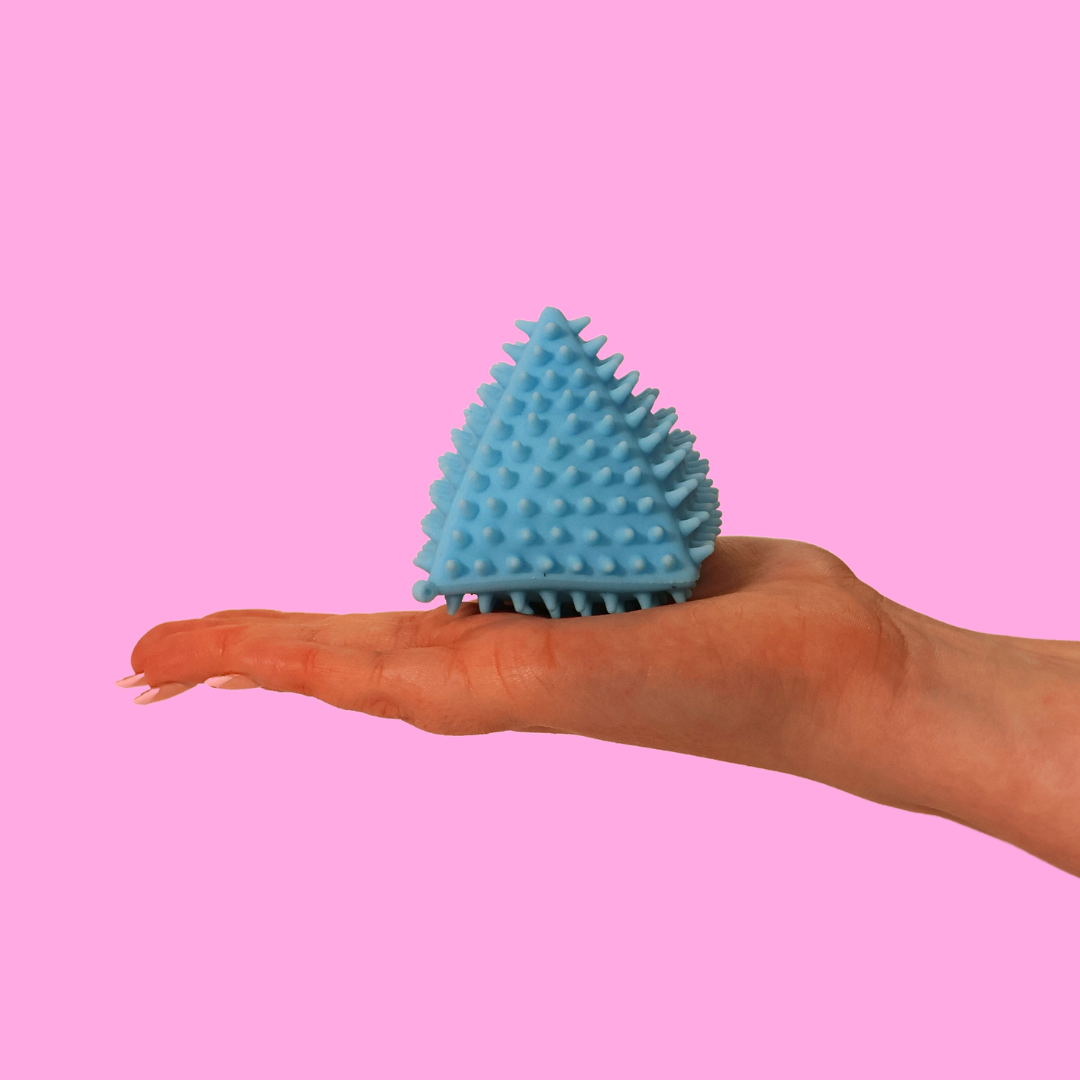 A hand holding a spiky blue triangle fidget toy against a pink background