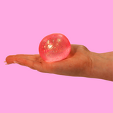 Pink sugar fidget toy in the shape of a ball, in the palm of a hand against a pink background