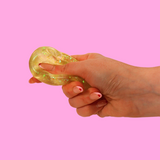 Yellow sugar fidget toy being squashed in a hand against a pink background