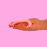 A pink, stretchy unicorn toy bracelet on a hand against a pink background.