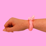 A hand wearing a pink unicorn spiky rubber bracelet on a pink background