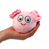 WHite background with a hand coming in from the side holding a pink round plush, it is an axolotl. It has a smiley face and pink fluffy ears