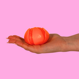 An orange fidget toy in the shape of a tangerine in the palm of a hand on a pink background